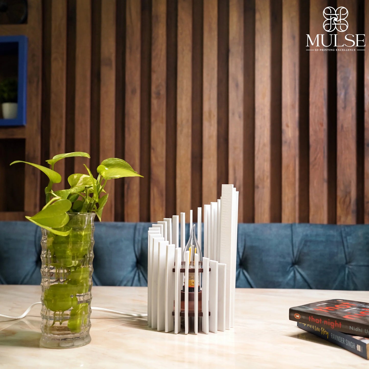 Modern white 3D printed table lamp, glass plant vase, books on marble table, wooden wall backdrop