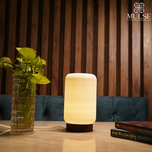 Modern table lamp with warm light beside a glass vase with green plant on wooden table