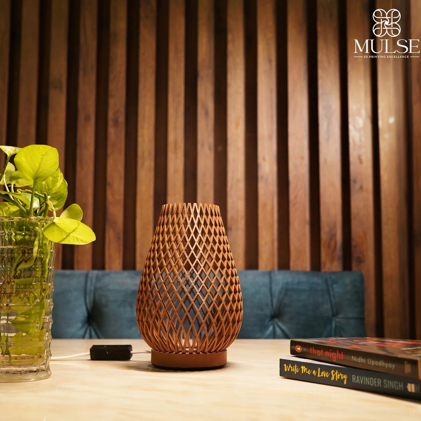 Modern 3D printed decorative lamp on table with houseplant, books, and wood panel backdrop