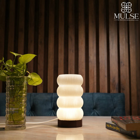 Modern 3D-printed table lamp with wavy design on wooden table beside green plant and books