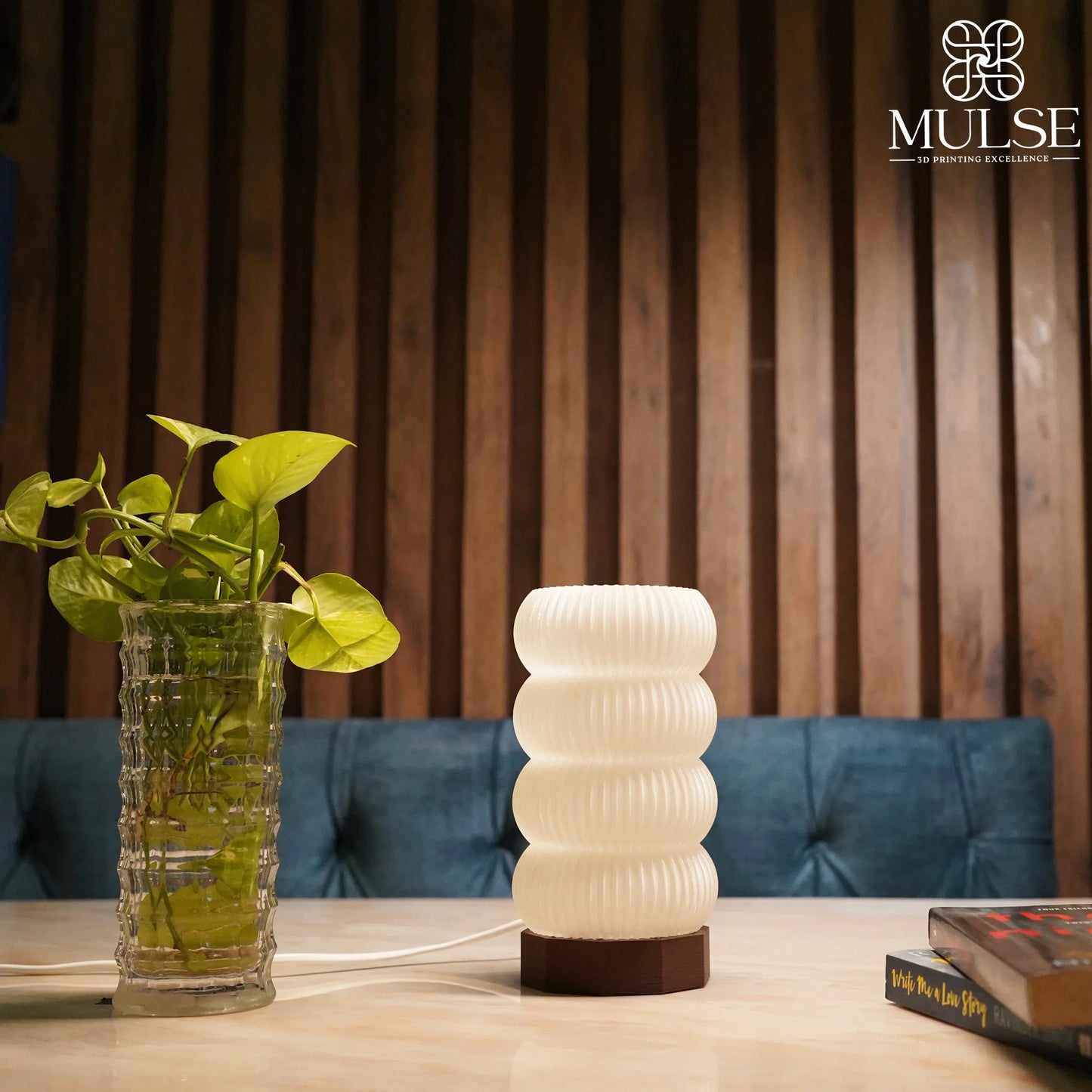 Modern ribbed table lamp with wooden base beside glass vase with green plant on marble table