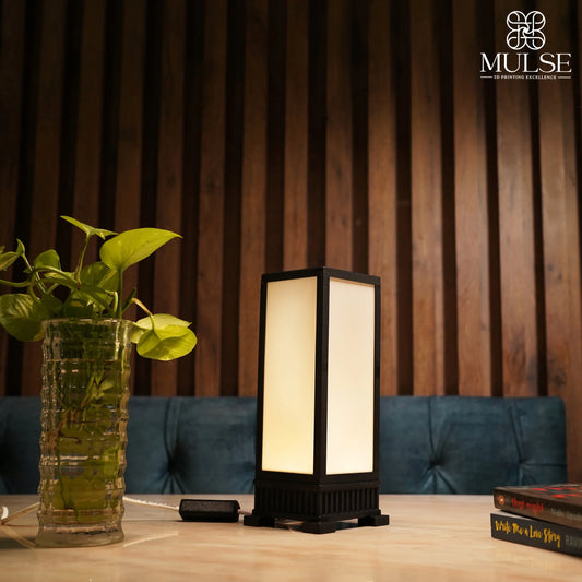Modern rectangular table lamp with soft warm light beside a green plant in a glass vase on a wooden surface