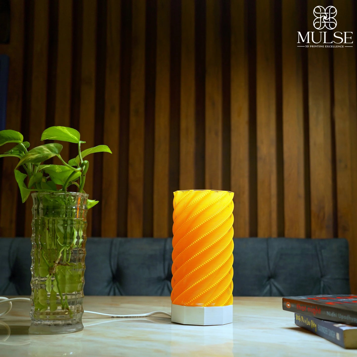 Modern yellow spiral 3D printed table lamp on marble surface beside a glass plant vase